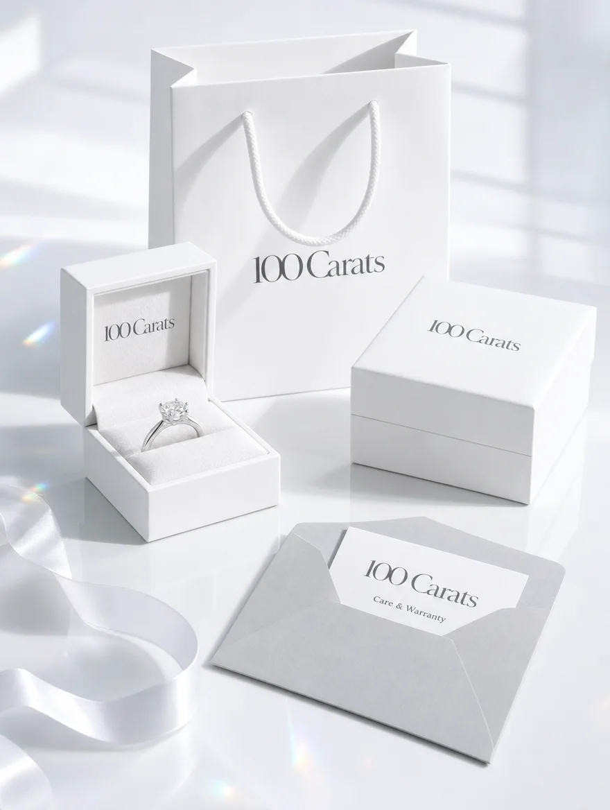 A white gold diamond ring in an open 100 Carats box, with a branded gift bag, gift box, ribbon, and a care card in a stationery envelope